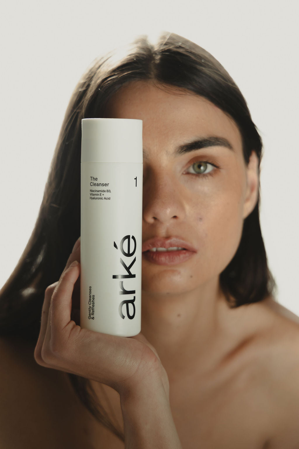 Woman holding arke cleanser in front of her face with a white background