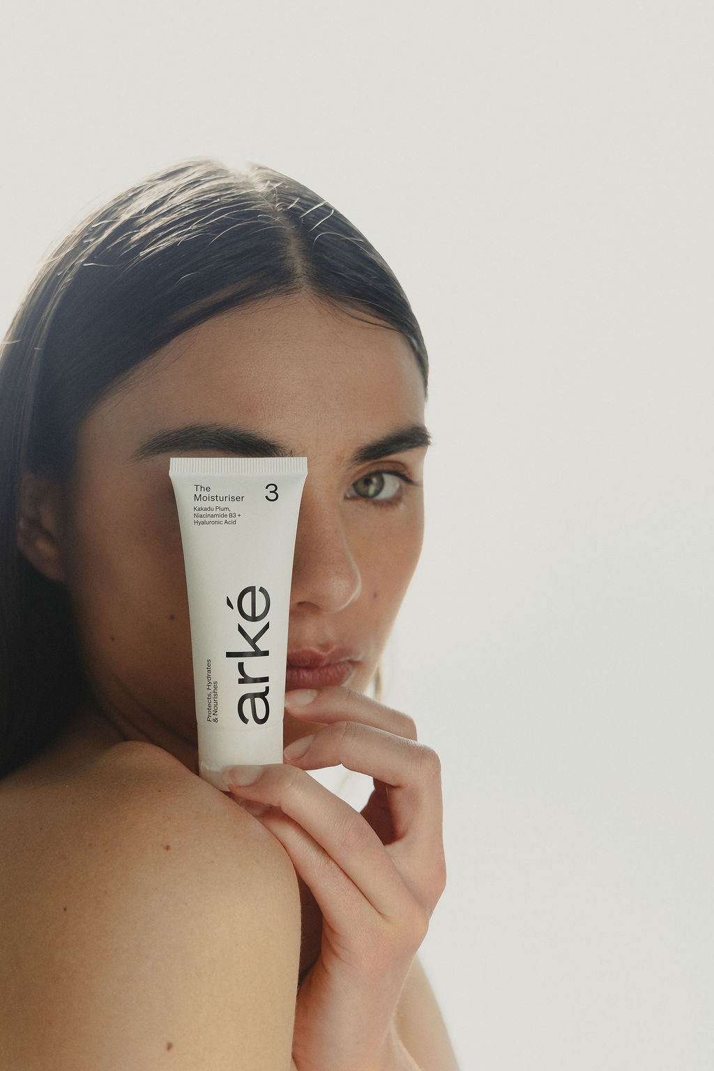 Woman holding arke moisturiser with a neutral background