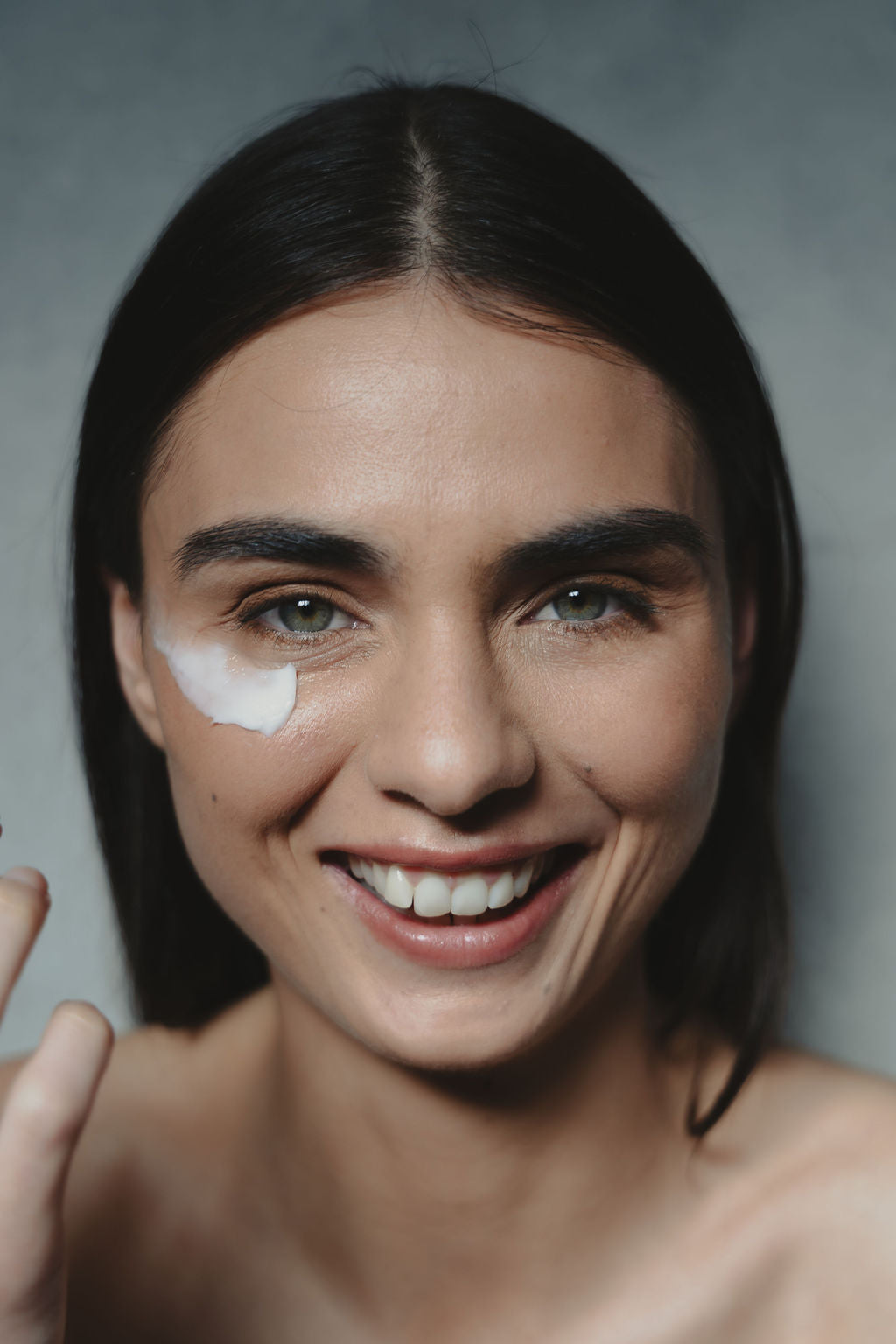 Woman with arke skincare product on her face against a gray background