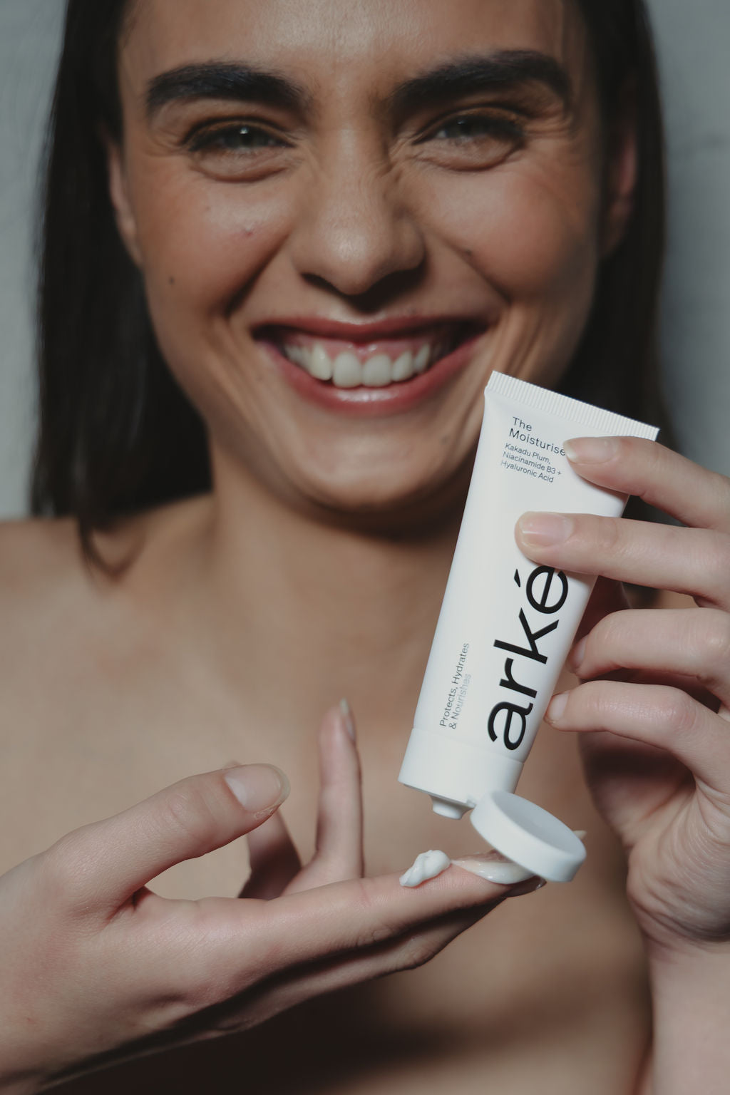 Woman holding arke moisturiser with a neutral background